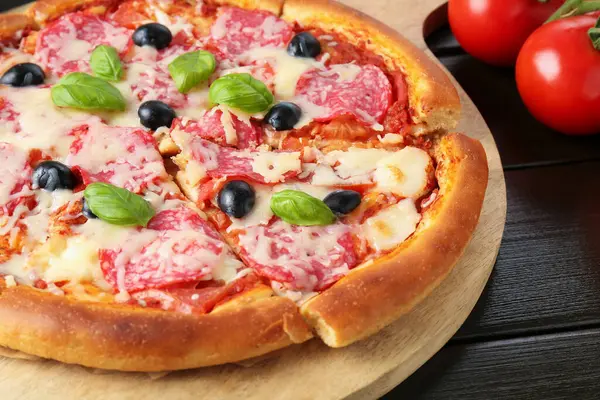 Siyah ahşap masada salamlı, peynirli, fesleğenli ve zeytinli lezzetli pizza.