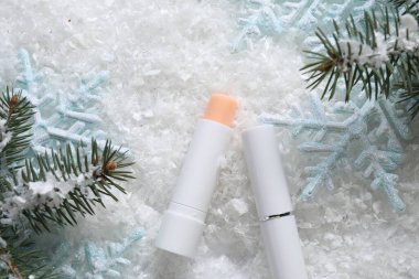 Nemlendirici dudak kremleri, Noel dekorasyonu ve yapay kar üzerindeki köknar ağacı dalları. Kış bakımı