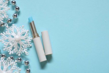 Nemlendirici dudak kremi ve açık mavi arka planda Noel dekoru, düz yatış. Metin için boşluk