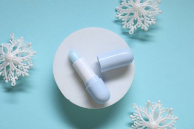 Nemlendirici dudak kremi ve açık mavi arka planda Noel dekoru, düz yatış. Kış bakımı