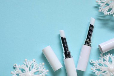 Nemlendirici dudak kremleri ve açık mavi arka planda Noel süslemeleri, düz yatış. Metin için boşluk