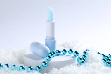 Nemlendirici dudak kremi ve yapay kar üzerine Noel süsü, yakın plan. Kış bakımı