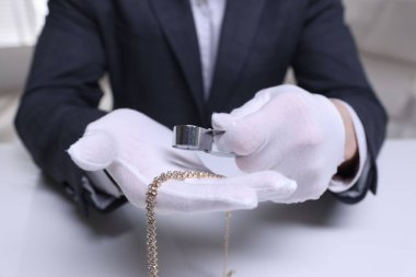 Beyaz masa içerisindeki lüks gerdanlığı değerlendiren eksper, yakın plan.