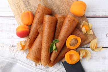 Lezzetli meyve dürümleri, kayısılar ve beyaz ahşap masa üzerinde bitki salatası, düz uzanış