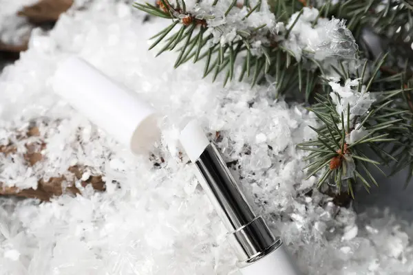 Nemlendirici dudak kremi ve suni kar üzerinde köknar ağacı dalları, yakın plan. Kış bakımı