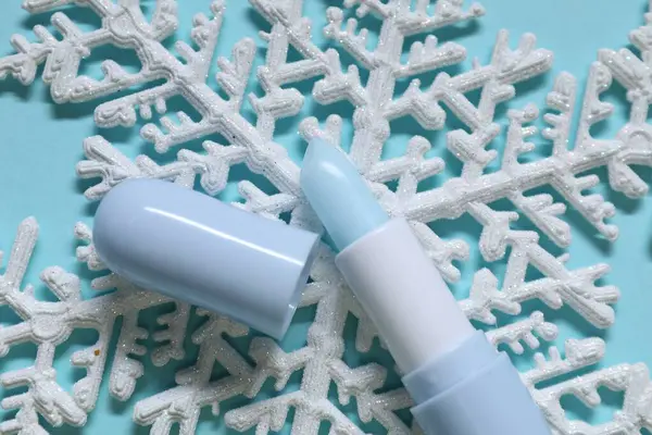 Nemlendirici dudak kremi ve açık mavi arka planda Noel dekoru, düz yatış. Kış bakımı