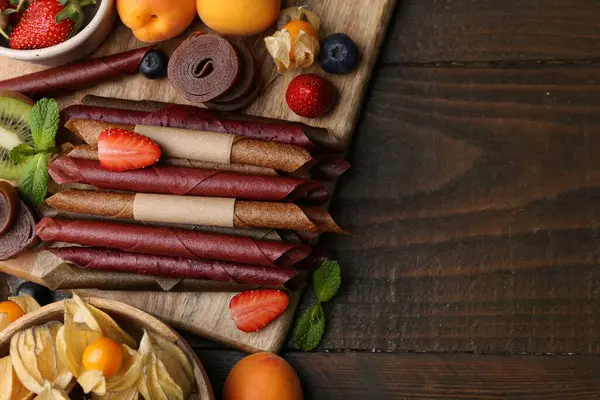 Lezzetli deri rulo şekerler, ahşap masada meyveler ve böğürtlenler, düz yatak. Metin için boşluk