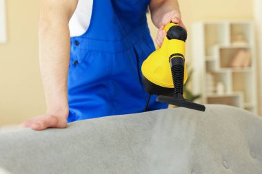 Temizlikçi kanepeyi evde buharlı temizleme makinesiyle temizliyor.