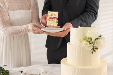 Damat, düğün pastasından bir parça tabağa koyuyor. Gelini masada kapalı tutuyor, yakın plan.