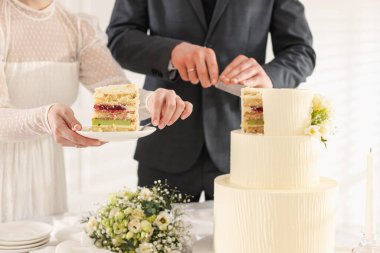 Yeni evliler kapalı bir masada düğün pastası kesiyorlar.