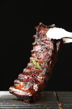 Siyah arka planda ızgaradan maşayla leziz domuz pirzolası alıp yakın plan çekiyoruz.