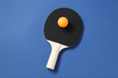 Mavi zemin üzerinde pinpon raketi ve top, üst görünüm