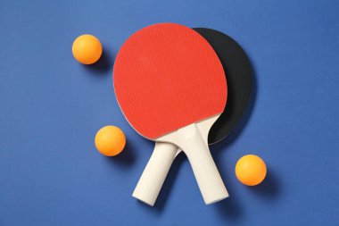 Masa tenisi raketleri ve topları mavi arkaplanda, üst görünümde.