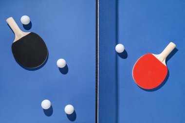 Masa tenisi raketleri, toplar ve ağ mavi arka planda, düz yatıyordu.