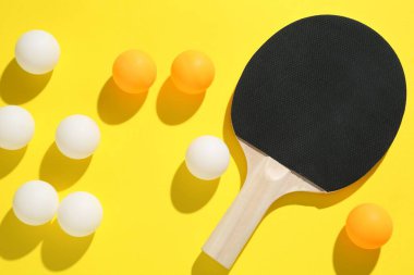 Masa tenisi raketi ve toplar sarı arka planda, düz yatıyordu