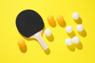 Masa tenisi raketi ve toplar sarı arka planda, düz yatıyordu
