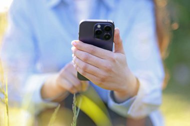 Güneşli bir günde akıllı telefondan bitki tanıma uygulaması kullanan bir kadın.