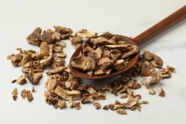 Beyaz masadaki kaşıkta kurumuş hindiba kökleri, yakın plan.