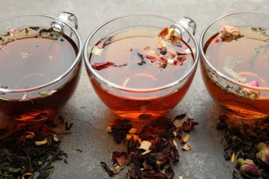 Cam fincanlarda aromatik bitki çayı ve gri masada kuru yapraklar, yakın plan.