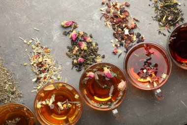 Cam fincanlarda aromatik bitki çayı, kuru yapraklar ve gri masada çiçekler, düz uzanmış