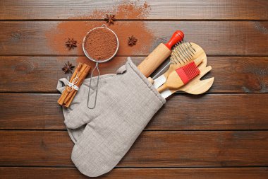 Farklı mutfak aletleri fırın eldivenlerinde, kakao tozu, tarçın ve anason yıldızları tahta masada, düz yerde