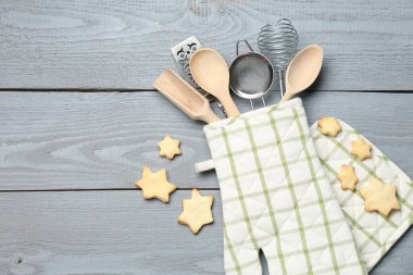 Fırın eldiveninde farklı mutfak aletleri ve açık gri ahşap masada yıldız şeklinde kurabiyeler. Metin için boşluk