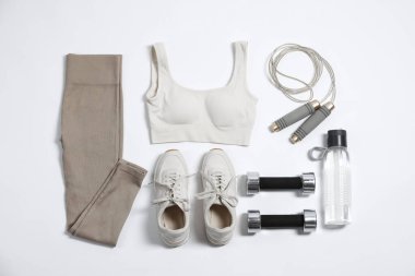 Spor kıyafetleri, spor ayakkabıları, dambıllar, atlayan ip ve su şişesi beyaz arka planda, düz yatıyordu.