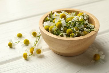 Taze papatya çiçekleri ve kase beyaz ahşap masada, yakın plan.