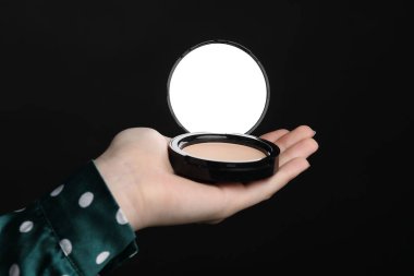 Siyah arka planda aynalı açık yüz pudrası tutan kadın, yakın plan.