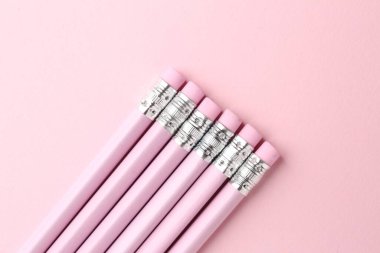 Pembe arka planda silgileri olan çizgili kalemler, düz konum