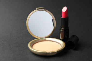 Aynalı açık yüz pudrası ve siyah arkaplanda ruj, yakın plan.