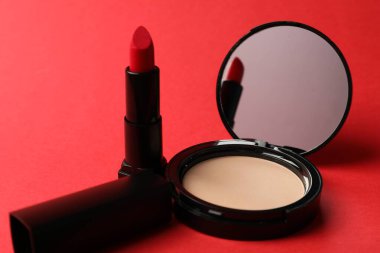 Aynalı açık yüz pudrası ve kırmızı arkaplanda ruj, yakın plan.