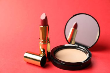 Aynalı açık yüz pudrası ve kırmızı arkaplanda ruj, yakın plan.