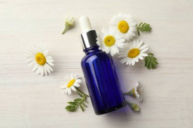 Bir şişe temel yağ ve papatya çiçekleri açık ahşap masa üzerinde, düz yatıyordu.