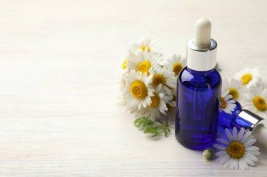 Hafif ahşap masada gerekli yağ şişeleri ve papatya çiçekleri, yakın plan. Metin için boşluk