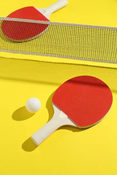 Sarı arka planda pinpon raketleri, top ve ağ.