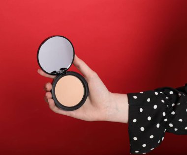 Kırmızı arka planda aynalı açık yüz pudrası tutan kadın, yakın plan.