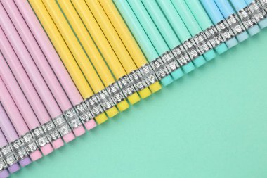 Turkuaz arka planda silgisi olan bir sürü grafit kalem, düz zemin. Metin için boşluk