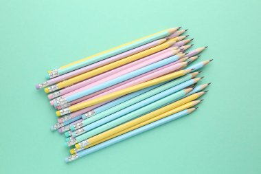 Turkuaz arka planda silgileri olan birçok grafit kalem, düz konum
