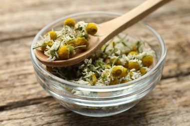 Kuru papatya çiçekleri kâsede ve kaşık tahta masada, yakın plan.