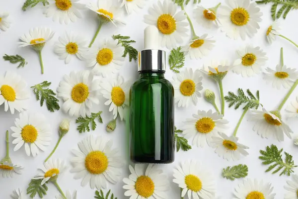 Beyaz arka planda bir şişe temel yağ ve papatya çiçeği.