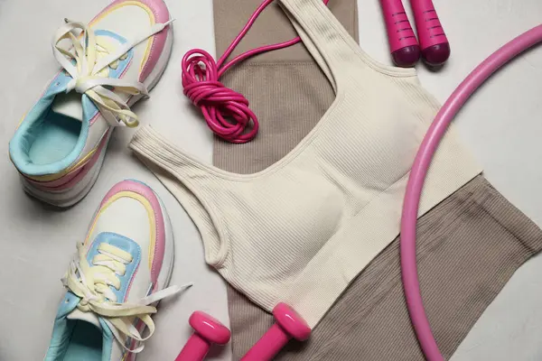 Spor kıyafetleri, spor ayakkabıları, hula hoop, ip atlama ve gri desenli arka planda dambıllar, düz uzanma