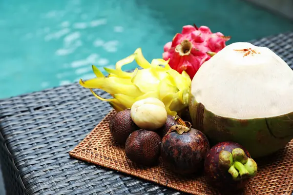 Yüzme havuzunun yakınındaki hasır masada farklı tropikal meyveler var. Metin için boşluk