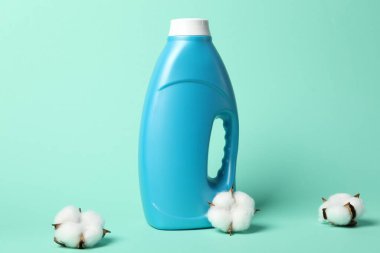 Bir şişe yumuşatıcı ve turkuaz arka planda pamuk çiçekleri.