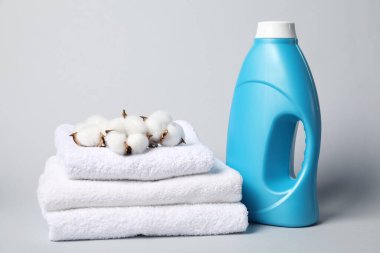 Açık gri arkaplanda bir şişe yumuşatıcı, havlu ve pamuk çiçeği.