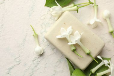 Bir kalıp sabun ve yasemin çiçekleri ışık masasında, düz yerde. Metin için boşluk