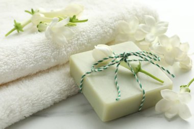 Bir kalıp sabun, yasemin çiçekleri ve beyaz mermer masaya havlu, yakın plan.