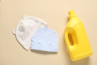 Bir şişe yumuşatıcı ve bej arka planda bebek şapkası.