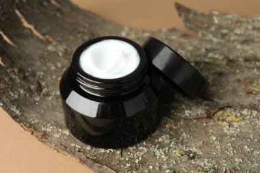 Bej arka planda vücut kremi ve ağaç kabuğu kavanozu, yakın plan.