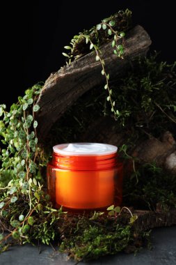 Kavanoz dolusu nemlendirici vücut kremi, ağaç kabuğu ve bitkiler gri masada, yakın plan.